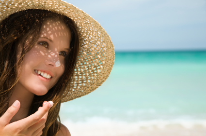 Woman on the beach with a straw hat on and sunscreen on her nose and finger