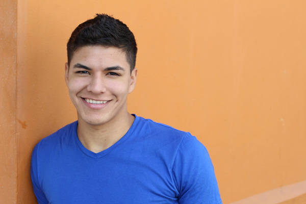 Young man smiling while leaning against a wall.