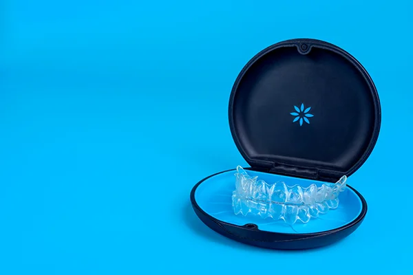 Set of clear aligners resting in an Invisalign® branded case on a blue background.