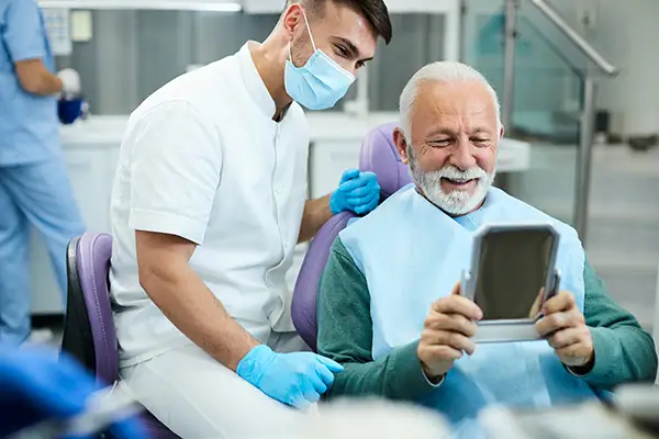 Happy, senior patient looking at themselves in a mirror with a pleased dental assistant.