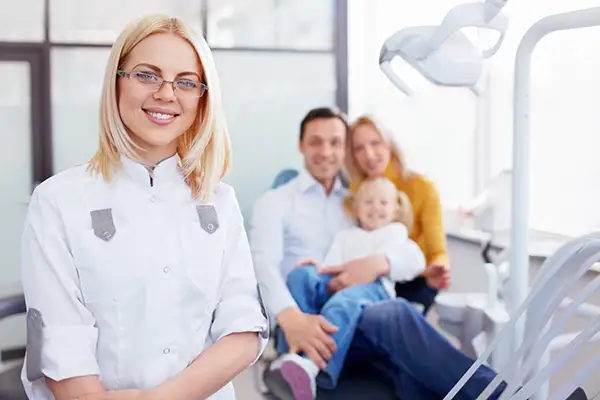 A female dentist standing with a family in a dental chair, representing the warm, welcoming environment of a family dental practice.